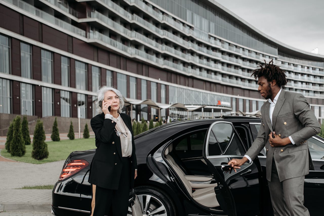 Man in a Gray Suit Opening a Car Door for a Woman in Black Suit